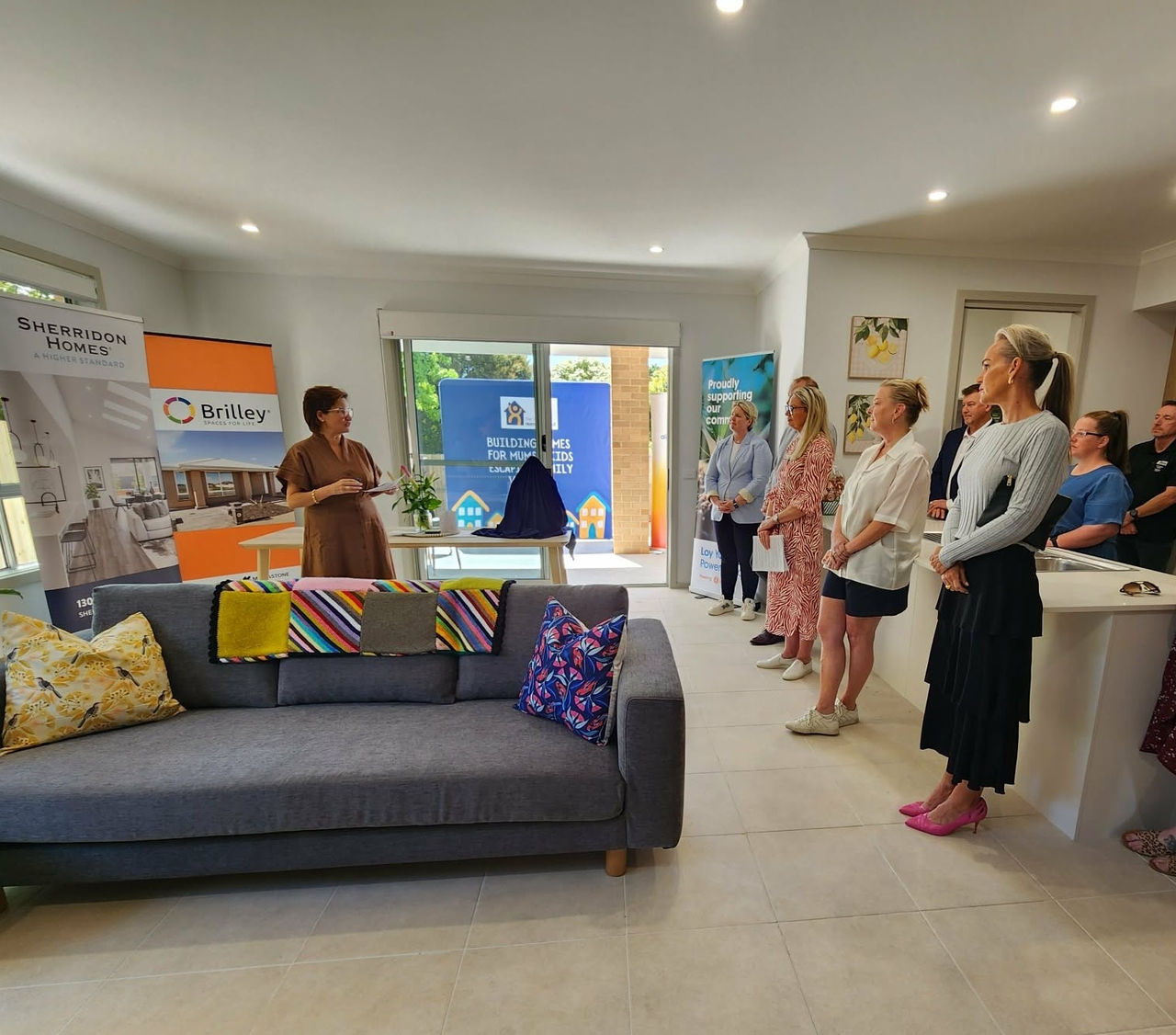 Several attendees of the opening of the house stand in a room.